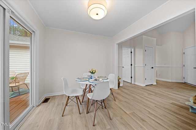 dining room with light wood finished floors, visible vents, baseboards, and crown molding