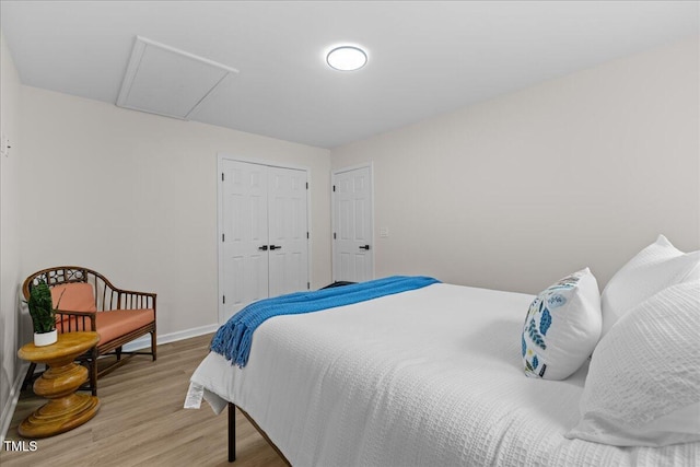 bedroom featuring light wood-style floors, attic access, baseboards, and a closet