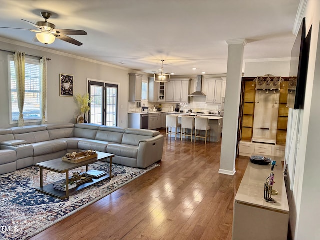 living area with decorative columns, ornamental molding, dark wood finished floors, and a ceiling fan