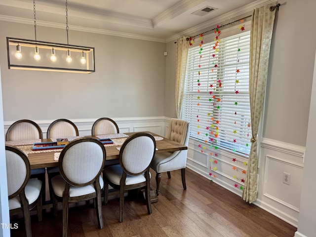 dining room with a tray ceiling, visible vents, ornamental molding, wainscoting, and wood finished floors