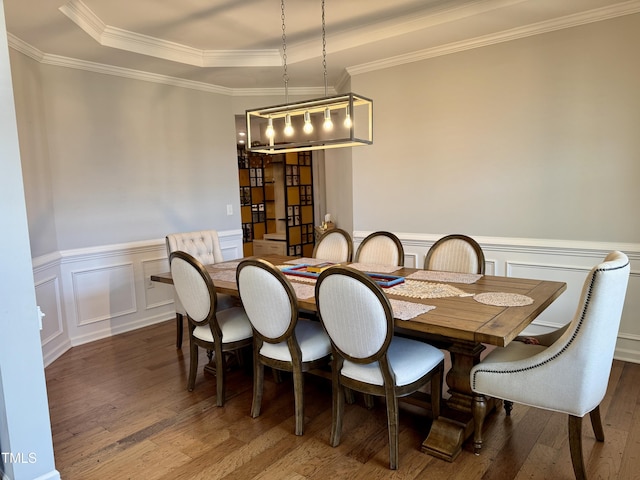 dining room with a raised ceiling, a wainscoted wall, crown molding, and wood finished floors