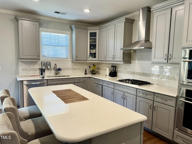 kitchen featuring gray cabinetry, stainless steel appliances, a breakfast bar, a sink, and wall chimney exhaust hood