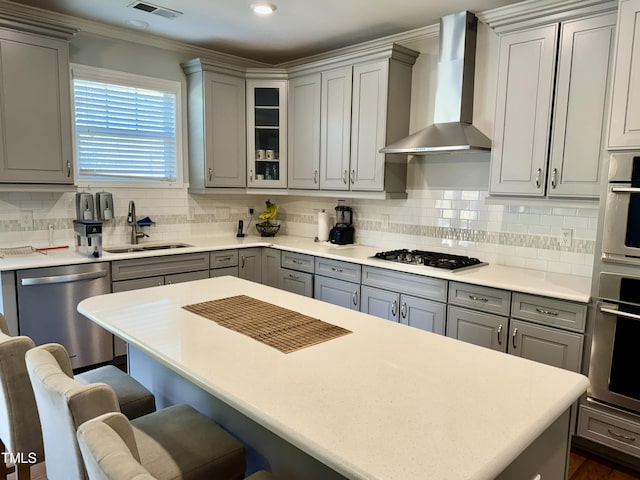 kitchen with stainless steel appliances, wall chimney range hood, a kitchen bar, and gray cabinets