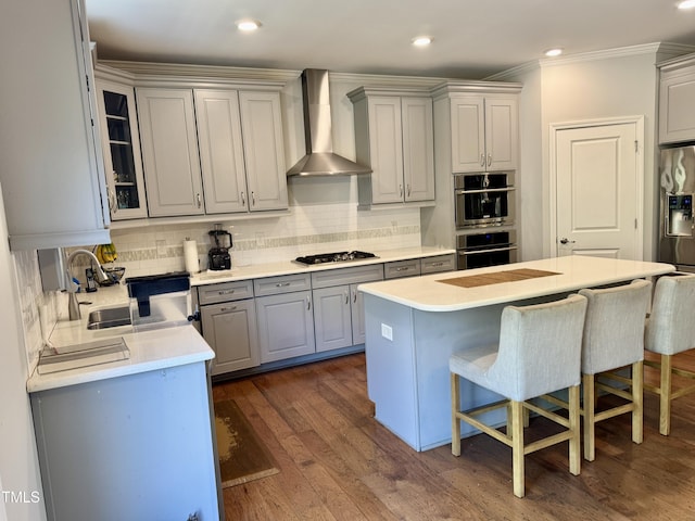 kitchen with wall chimney exhaust hood, a kitchen breakfast bar, gray cabinets, stainless steel appliances, and a sink