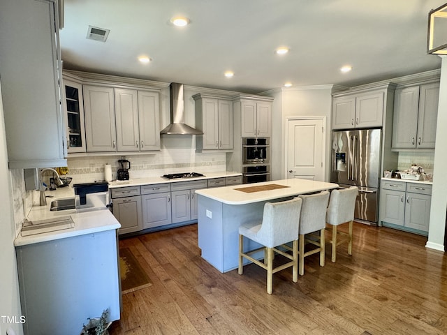 kitchen featuring visible vents, appliances with stainless steel finishes, gray cabinets, a center island, and wall chimney exhaust hood