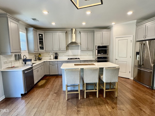 kitchen with gray cabinets, visible vents, appliances with stainless steel finishes, a sink, and wall chimney range hood