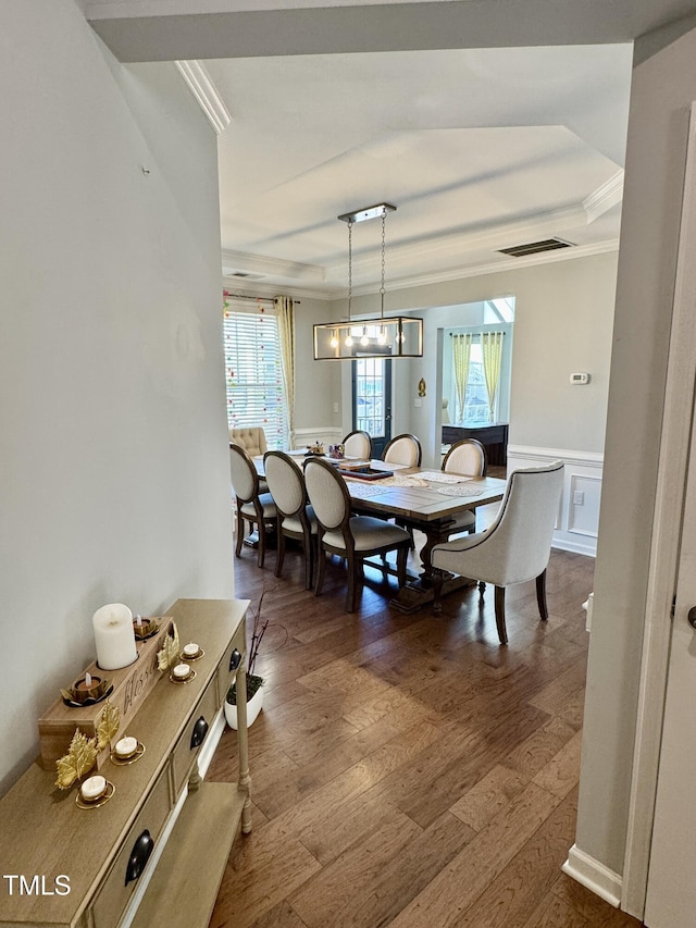 dining area with a wainscoted wall, dark wood finished floors, visible vents, an inviting chandelier, and ornamental molding