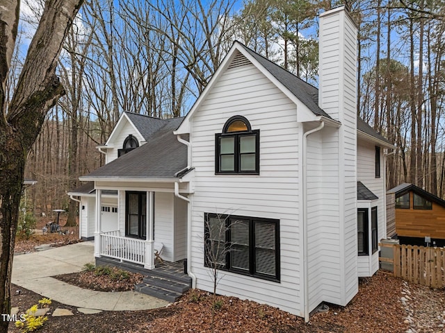 view of front facade featuring a porch, roof with shingles, concrete driveway, a garage, and a chimney