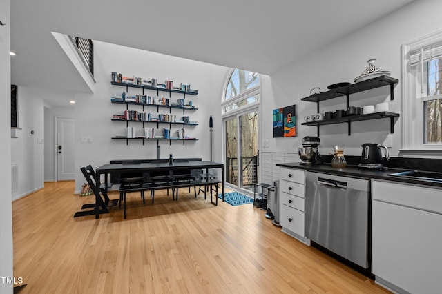 interior space with open shelves, stainless steel dishwasher, dark countertops, light wood-style floors, and a healthy amount of sunlight