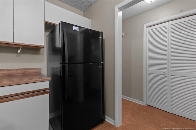 kitchen with a textured ceiling, baseboards, freestanding refrigerator, and white cabinetry