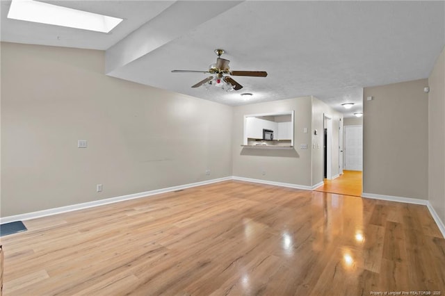 unfurnished living room with light wood-type flooring, a skylight, a ceiling fan, and baseboards