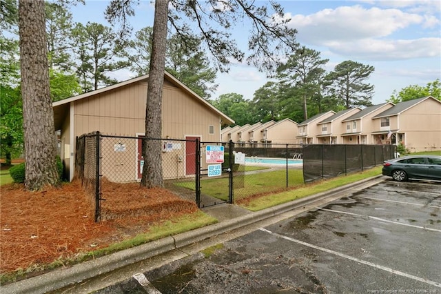 exterior space featuring uncovered parking, a gate, fence, a community pool, and a residential view