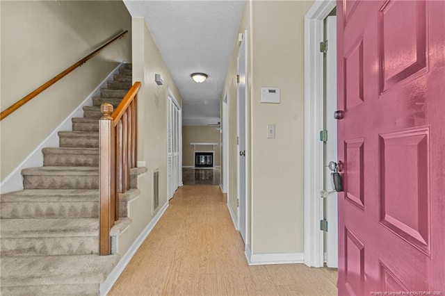 foyer entrance featuring visible vents, baseboards, a glass covered fireplace, light wood-style flooring, and stairway