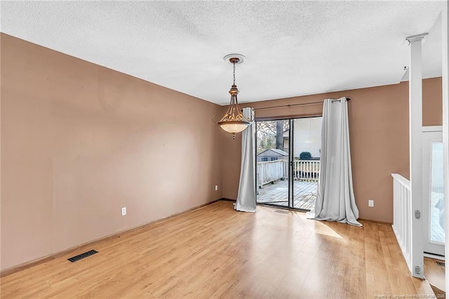 unfurnished room with light wood-style floors, visible vents, and a textured ceiling