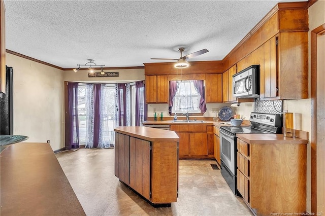 kitchen with a center island, brown cabinets, crown molding, appliances with stainless steel finishes, and a sink