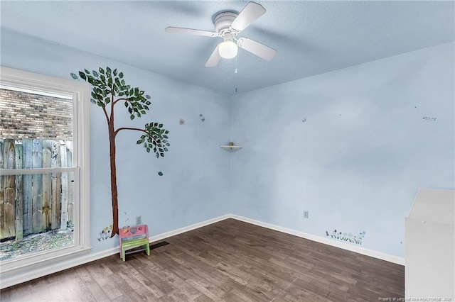 empty room with wood finished floors, a ceiling fan, and baseboards