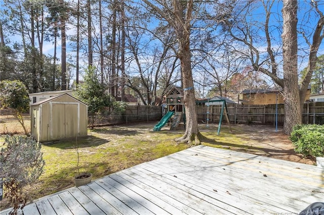 deck featuring a storage shed, a fenced backyard, a playground, and an outbuilding