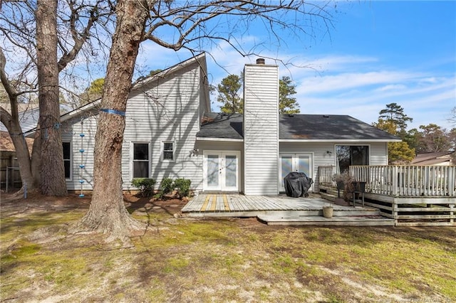 rear view of house featuring french doors, a chimney, a wooden deck, and a lawn