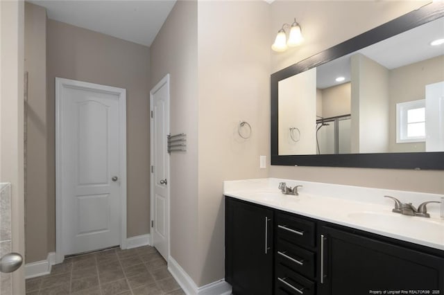 full bathroom with double vanity, a shower, a sink, and baseboards