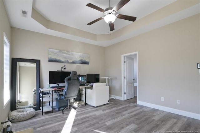 office featuring wood finished floors, a ceiling fan, visible vents, baseboards, and a tray ceiling