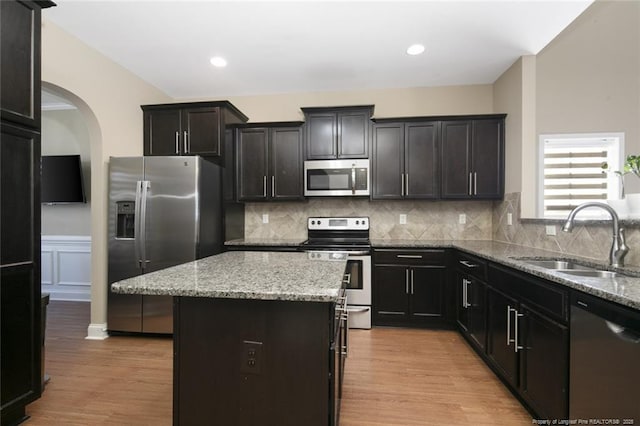 kitchen with light stone counters, a center island, stainless steel appliances, light wood-type flooring, and a sink