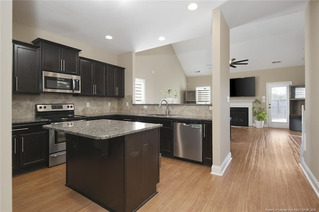 kitchen with ceiling fan, a kitchen island, appliances with stainless steel finishes, vaulted ceiling, and a sink