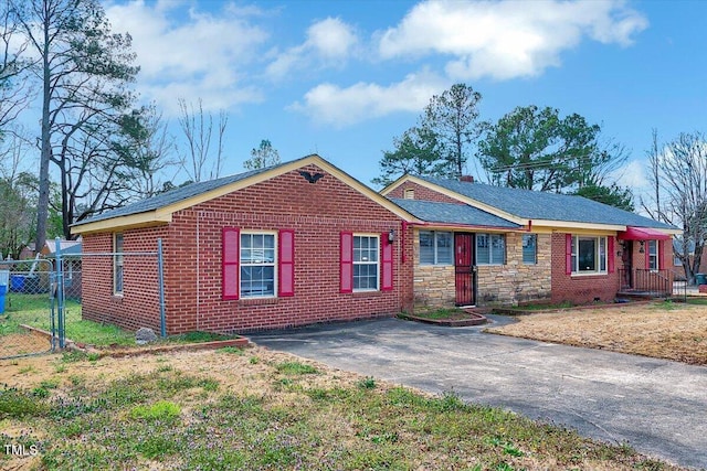 ranch-style house featuring aphalt driveway, brick siding, fence, stone siding, and a gate