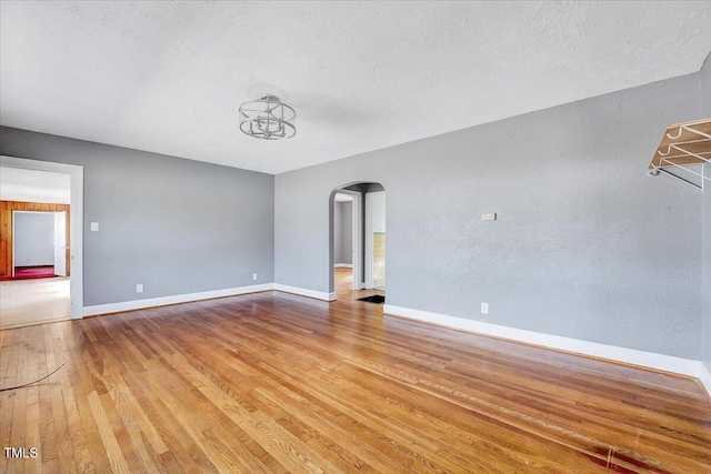 empty room with arched walkways, wood-type flooring, a textured ceiling, and baseboards