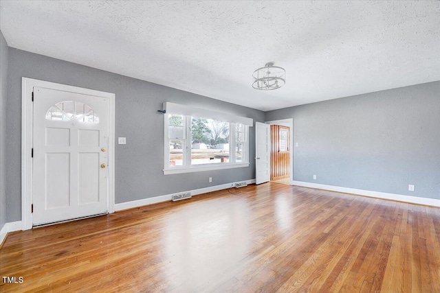 entryway with a textured ceiling, wood finished floors, visible vents, and baseboards