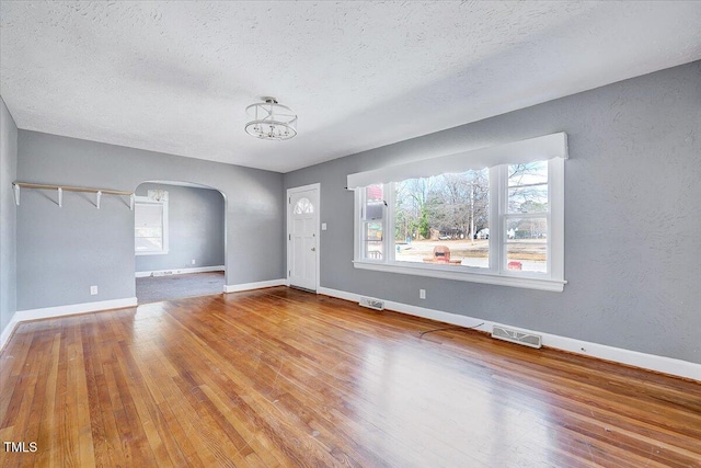 foyer entrance featuring baseboards, visible vents, arched walkways, hardwood / wood-style floors, and a textured ceiling