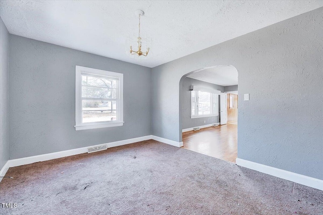 carpeted spare room featuring arched walkways, a textured wall, a textured ceiling, visible vents, and baseboards