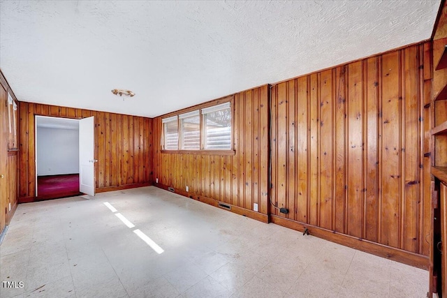 empty room with a textured ceiling, wooden walls, baseboards, and tile patterned floors