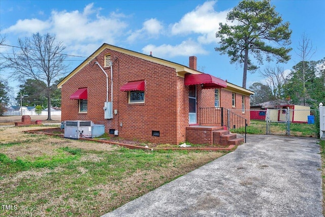 view of side of home featuring central AC unit, brick siding, crawl space, a gate, and a chimney