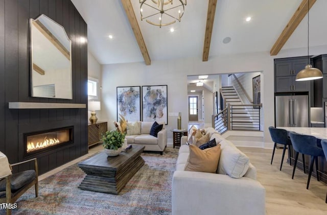 living room with lofted ceiling with beams, a chandelier, a large fireplace, light wood-style floors, and stairs