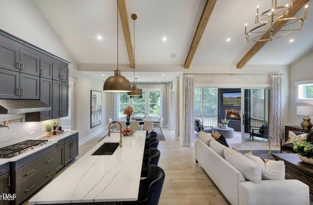 kitchen with lofted ceiling with beams, open floor plan, under cabinet range hood, stainless steel gas cooktop, and a sink