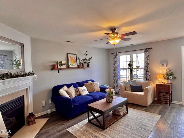 living area with visible vents, a fireplace with flush hearth, a ceiling fan, wood finished floors, and baseboards