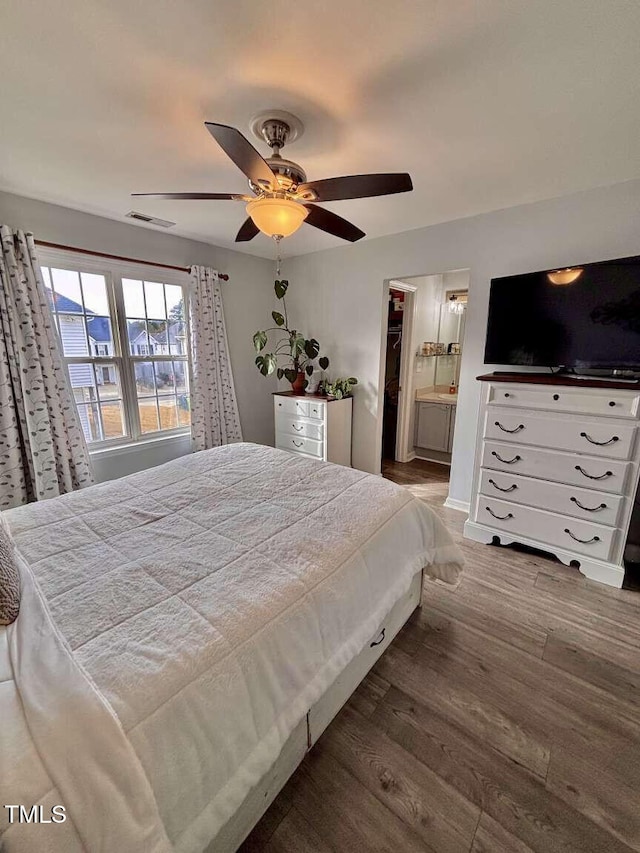 bedroom featuring visible vents, a ceiling fan, connected bathroom, wood finished floors, and baseboards