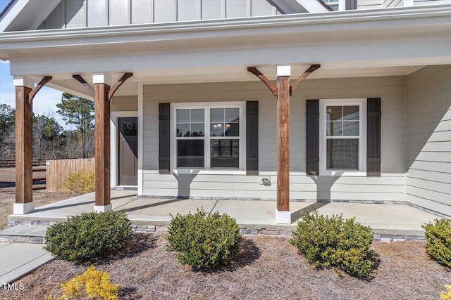 doorway to property featuring board and batten siding, a porch, and fence