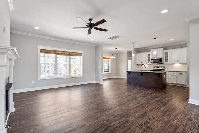 unfurnished living room featuring dark wood-type flooring, a sink, visible vents, baseboards, and crown molding