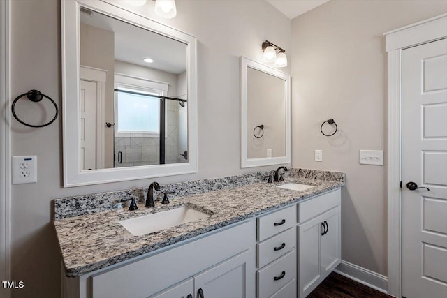 bathroom with double vanity, baseboards, a tile shower, and a sink