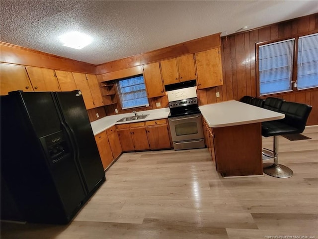 kitchen with electric stove, a peninsula, light countertops, black fridge, and a sink