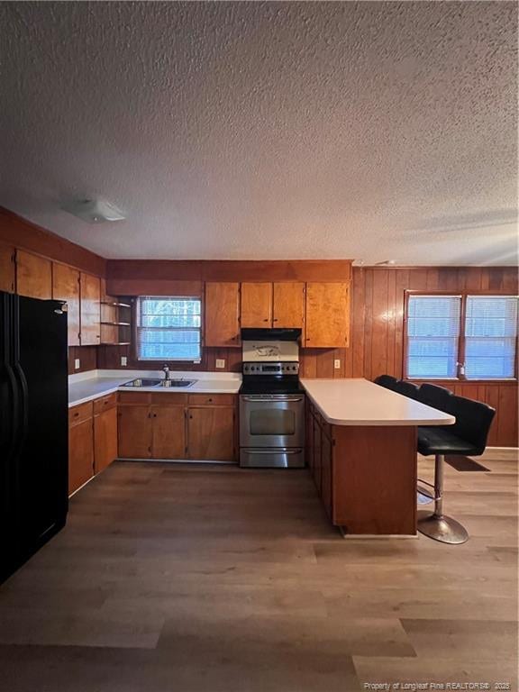 kitchen with electric range, brown cabinetry, freestanding refrigerator, a sink, and a peninsula