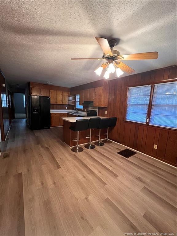 kitchen with visible vents, a peninsula, black fridge with ice dispenser, and light wood-style flooring