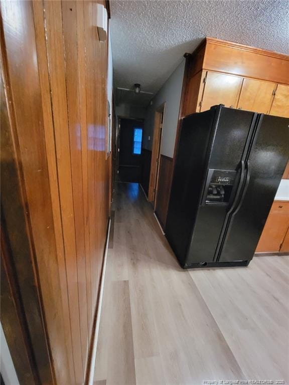 kitchen with a textured ceiling, light wood finished floors, and black fridge