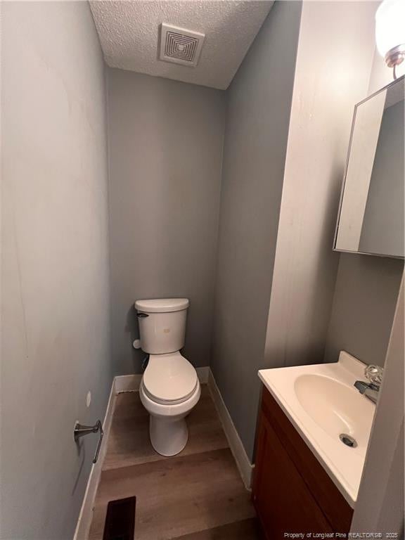 bathroom featuring visible vents, toilet, a textured ceiling, vanity, and wood finished floors