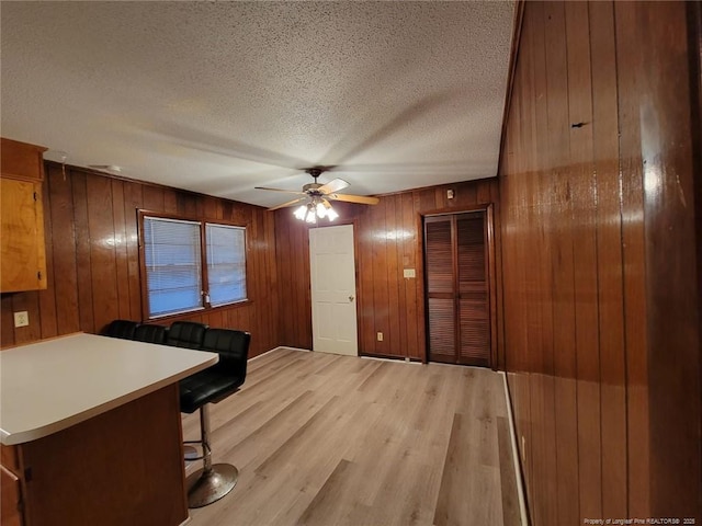 interior space with light wood-style floors, a ceiling fan, a textured ceiling, and wood walls