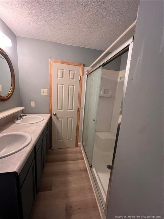 full bathroom featuring a textured ceiling, wood finished floors, a sink, and a shower stall