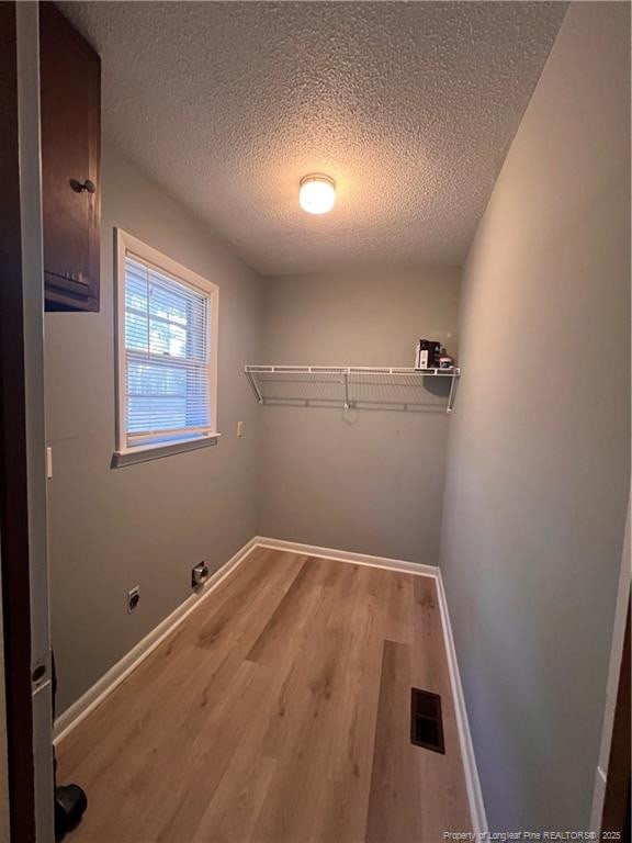 laundry room with a textured ceiling, laundry area, wood finished floors, visible vents, and baseboards