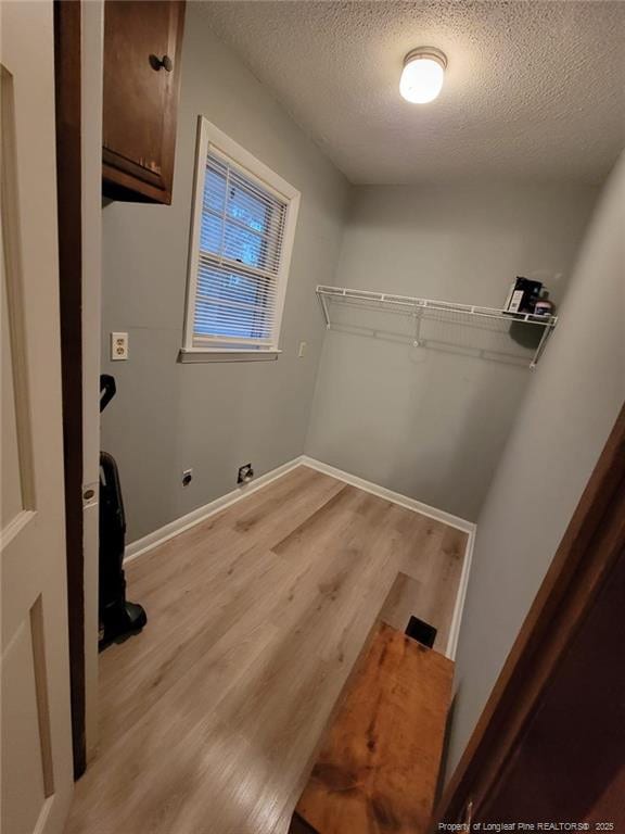 laundry area featuring cabinet space, light wood-style flooring, baseboards, and a textured ceiling