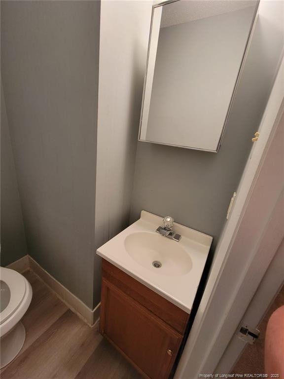 bathroom with toilet, baseboards, wood finished floors, and vanity